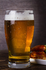 Glass of beer and chicken wings on dark wooden background