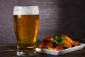 Glass of beer and chicken wings on dark wooden background