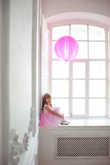 LIttle princess sitting on windowsill holding blloon in room. Alone girl. Childhood. 