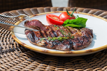 stages of cooking steak on the grill - ready piece of grilled steak on a plate with tomatoes and herbs on a table in a restaurant