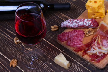 Glass and bottle of red wine, cheese, salami, walnuts, prosciutto and rosemary on wooden background. Still life