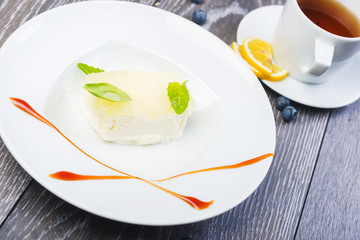 piece of Creamy vanilla ice cream with jelly and mint leaves on a white plate on a wooden table with decor and tea