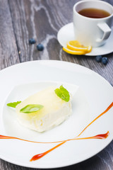 piece of Creamy vanilla ice cream with jelly and mint leaves on a white plate on a wooden table with decor and tea
