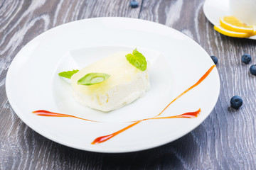 piece of Creamy vanilla ice cream with jelly and mint leaves on a white plate on a wooden table with decor and tea