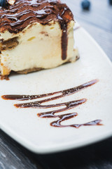 A tiramisu and a cup of tea on the white plate with blueberries and a mint on the woden table