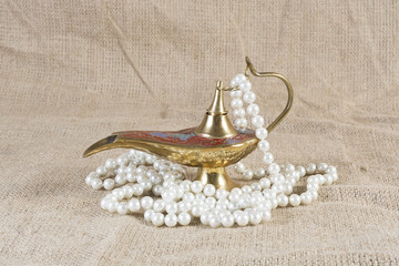 Moroccan brass oil lamp with pearl necklace on a burlap canvas