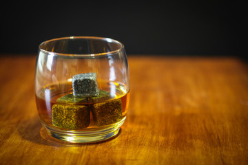 A glass of whiskey on the rocks in simple glass ware with whiskey stones on top a wood desk.