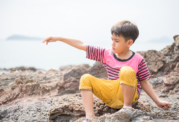 Fototapeta na wymiar Little boy sitting on the rock on the beach