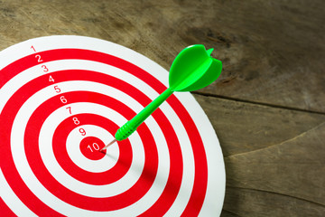 Green darts arrows in the target center on wooden background. Su