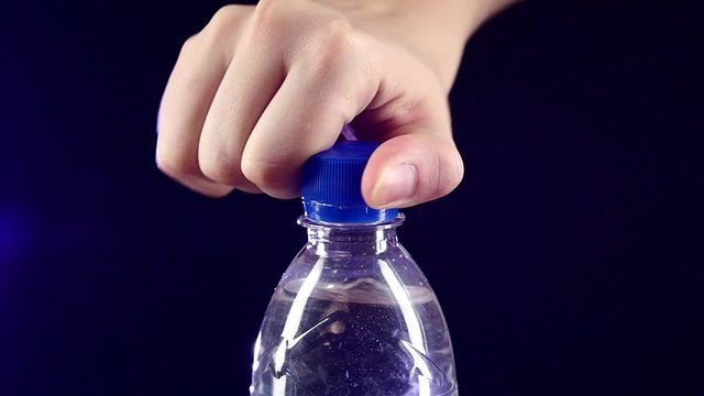 Hands opening a blue bottle of fresh water on dark, slow motion, splash, spray, bubbles