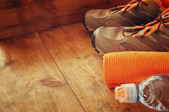 fitness concept with bottle of water, towel and sport footwear over wooden background
