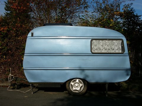 Fototapeta Alter Wohnwagen in Blau Metallic mit Gardine aus weißer Spitze für Vanlife und Camping am Straßenrand im Stadtteil Schildesche in Bielefeld im Teutoburger Wald in Ostwestfalen-Lippe