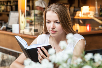 smiling girl sitting at summer terrace and reading book