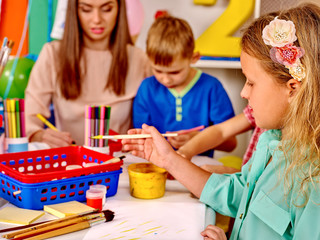 Kids with teacher holding colored paper and glue on table in kindergarten