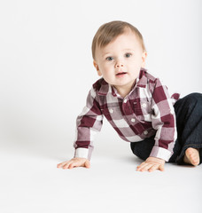 a cute 1 year old baby stands in white studio with jeans and a red white flannel looking camera left in excitement