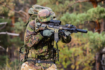 Gunner aims in forest/British soldier with military backpack aiming from his rifle in forest