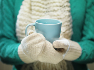  Woman hands in white woolen mittens holding a cozy cup with hot cocoa, tea or coffee. Winter and Christmas time concept.