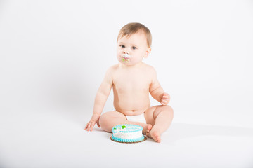 a cute 1 year old sits in a white studio setting. The boy is very excited to start eating his birthday cake. He is only dressed in a white diaper