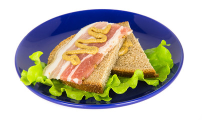 Bacon and mustard sandwich on a lettuce leaf lies on a blue plat