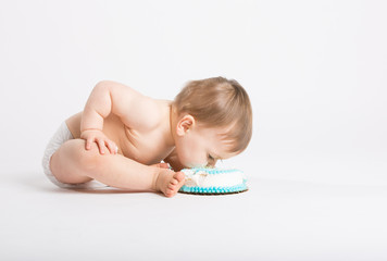 a cute 1 year old sits in a white studio setting. The boy bends in with hands on his legs and eats the cake with his face. He is only dressed in a white diaper