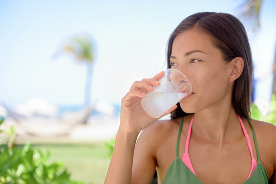Young woman drinking fresh water or lime juice at beach. Female is looking away while sitting at outdoor restaurant. Beautiful tourist is having healthy drink during summer vacation.