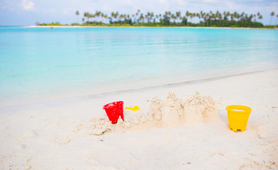 Sandcastle at white beach with plastic kids toys on perfect island