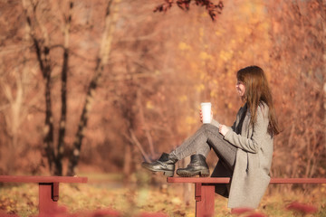 Fototapeta na wymiar Fall concept - beautiful woman drinking coffee in autumn park under fall foliage