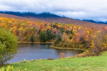 Fototapeta na wymiar fields and pond with hills in full fall color as fog moves in 