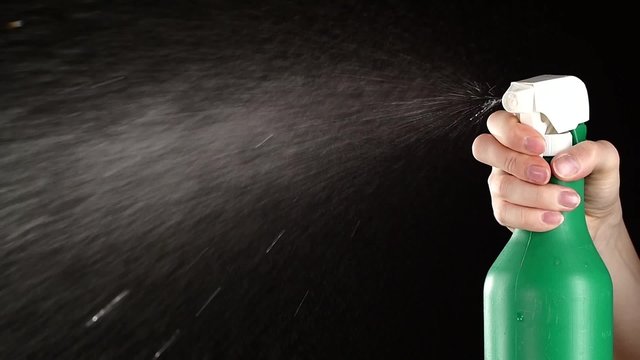 Hand holds spray bottle, on black, slow motion