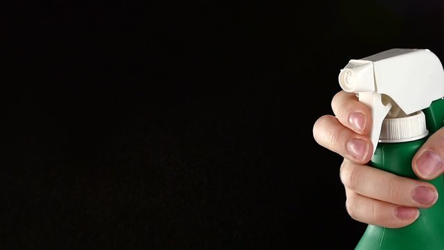 Hand holds spray bottle, on black, slow motion, close up