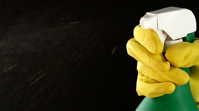 Hand in glove holds spray bottle, on black, slow motion, close up