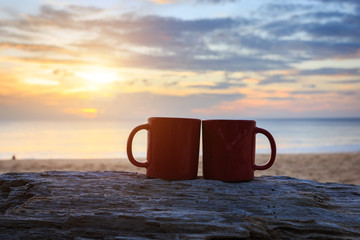 Coffee cup on wood log at sunset or sunrise beach