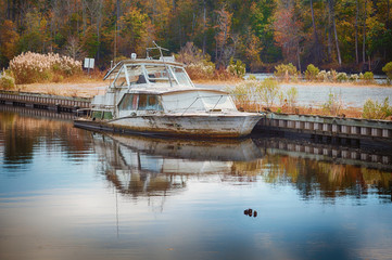 Old Abandoned Boat sinking at the pier with an autumn landscape in the background.