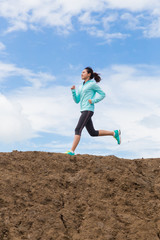 young woman running on trail with blue sky background