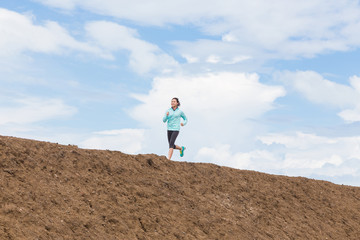 young woman running on trail with blue sky background
