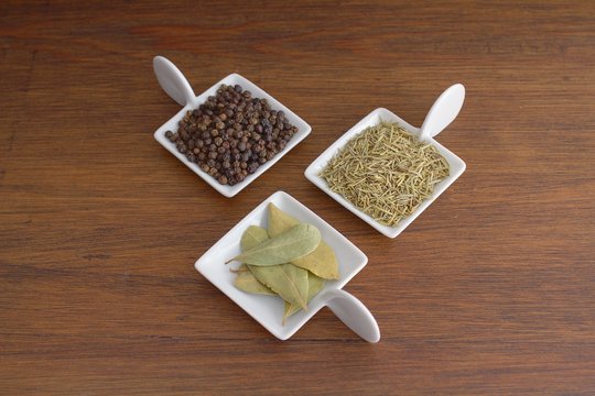 View of small plates of pepper berries, dried rosemary and bay leaves from above
