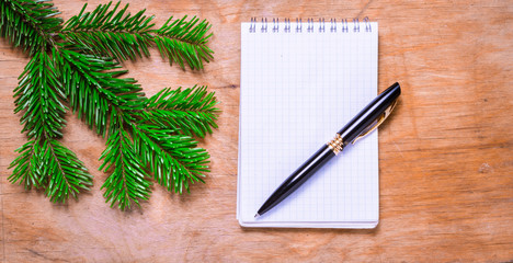 Pen and Notepad on old rustic table decorated with a fir branch.