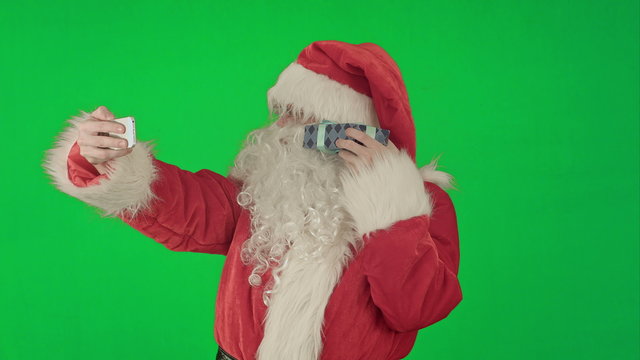 Santa Claus holding a big present  doing a selfie on smartphone on a Green Screen Chrome Key