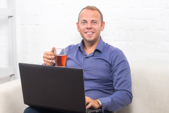 Handsome businessman sitting on couch with laptop at home in the living room, looking camera.