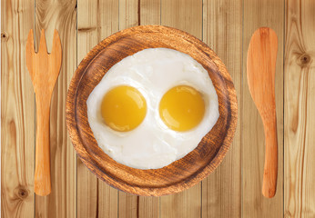 two fried eggs on wooden plate, knife and fork on wooden table
