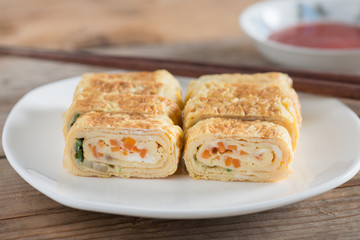 Japanese snack - eggs roll with carrot and onion on white plate.