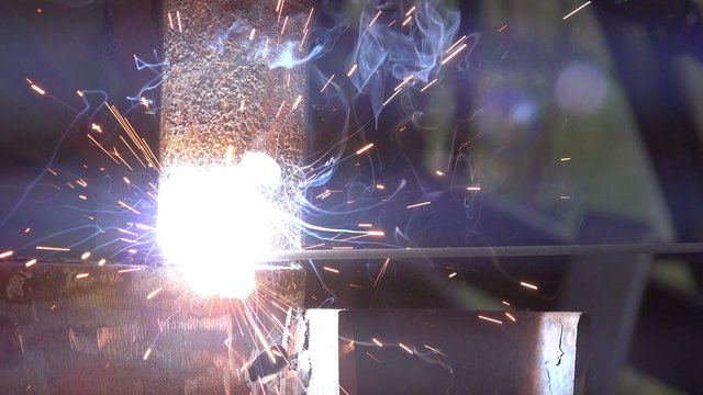 Close up macro footage of shielded metal arc welding in workshop, male welder using electrode to melt the metal at the welding point.