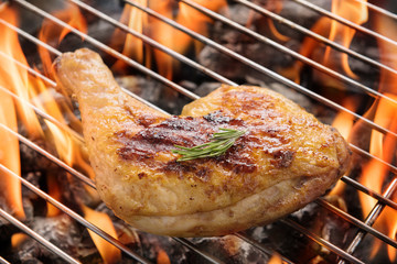 Chicken leg grilling over flames on a barbecue