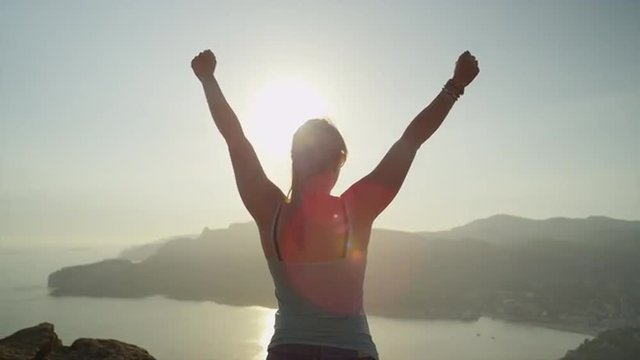 Woman reaches top of the mountain and raises her arms
