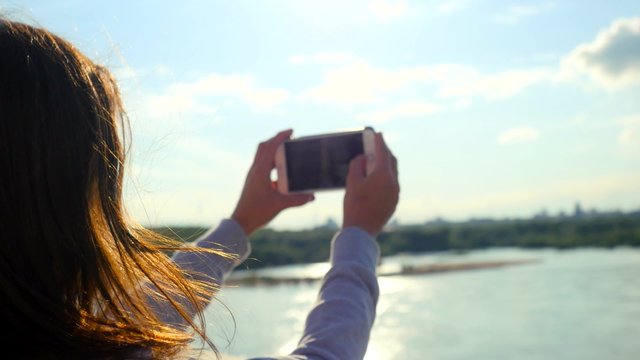 Beautiful woman taking pictures of her self, instagram, selfie on the bridge in sunny day at blurred nature background. The sun shines through her hair