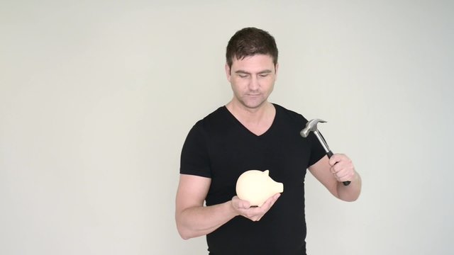 Man in casual dress holding piggy bank and hammer. He resist the impulse to break it.