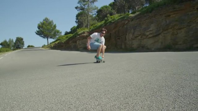 SLOW MOTION: Young man longboarding down the winding road
