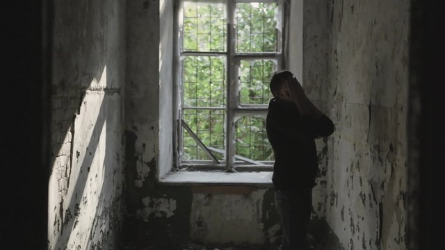 Young man in an abandoned house is upset , nervous / Young man in despair goes to an abandoned house, depressed
