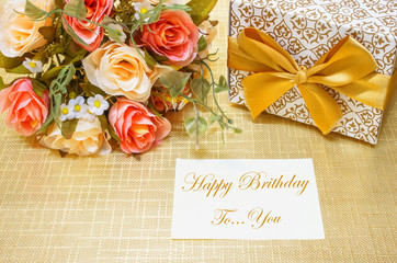Happy Birthday sign on paper note and decorate with flower and gift box on gold paper background