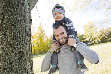 Portrait of happy father giving son piggyback ride on his shoulders in autumn park